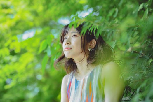 Smiling young woman with short brown hair in nature, surrounded by lush green leaves.