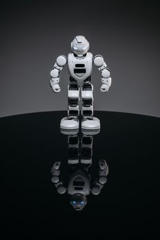 A modern robot with glowing eyes standing and reflecting on a glossy surface.