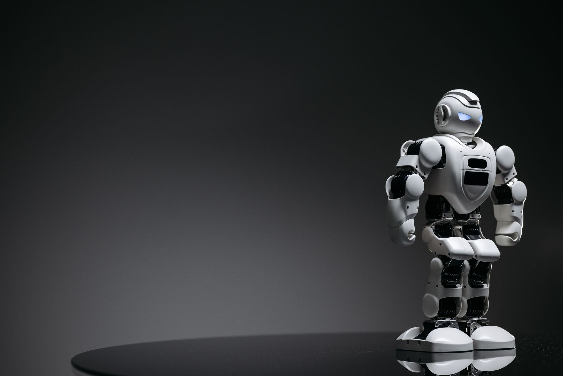 Compact humanoid robot toy standing on a reflective surface, exuding a futuristic vibe.