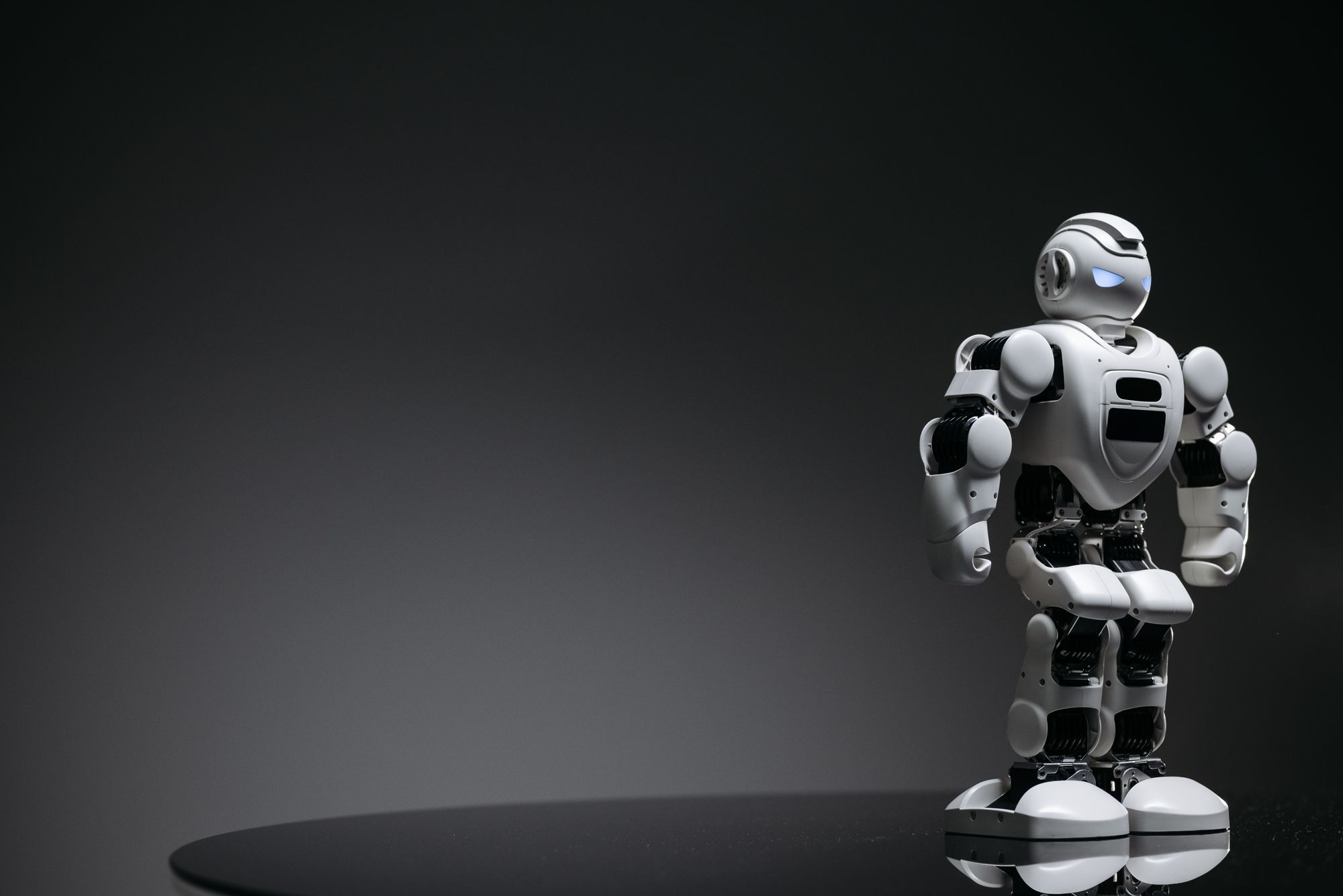 Compact humanoid robot toy standing on a reflective surface, exuding a futuristic vibe.