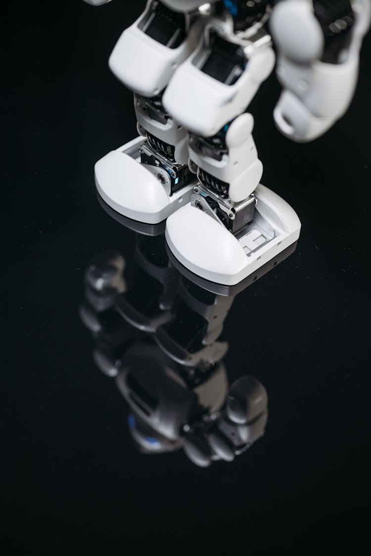 Knee And Feet Of A White Robot Standing On A Black Shiny Surface