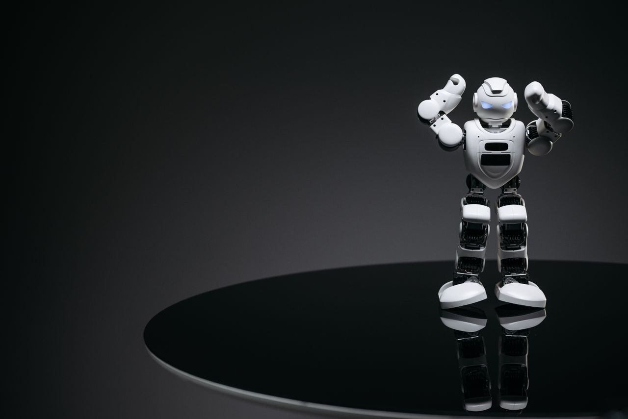 a small humanoid robot with glowing eyes on a reflective table in a da