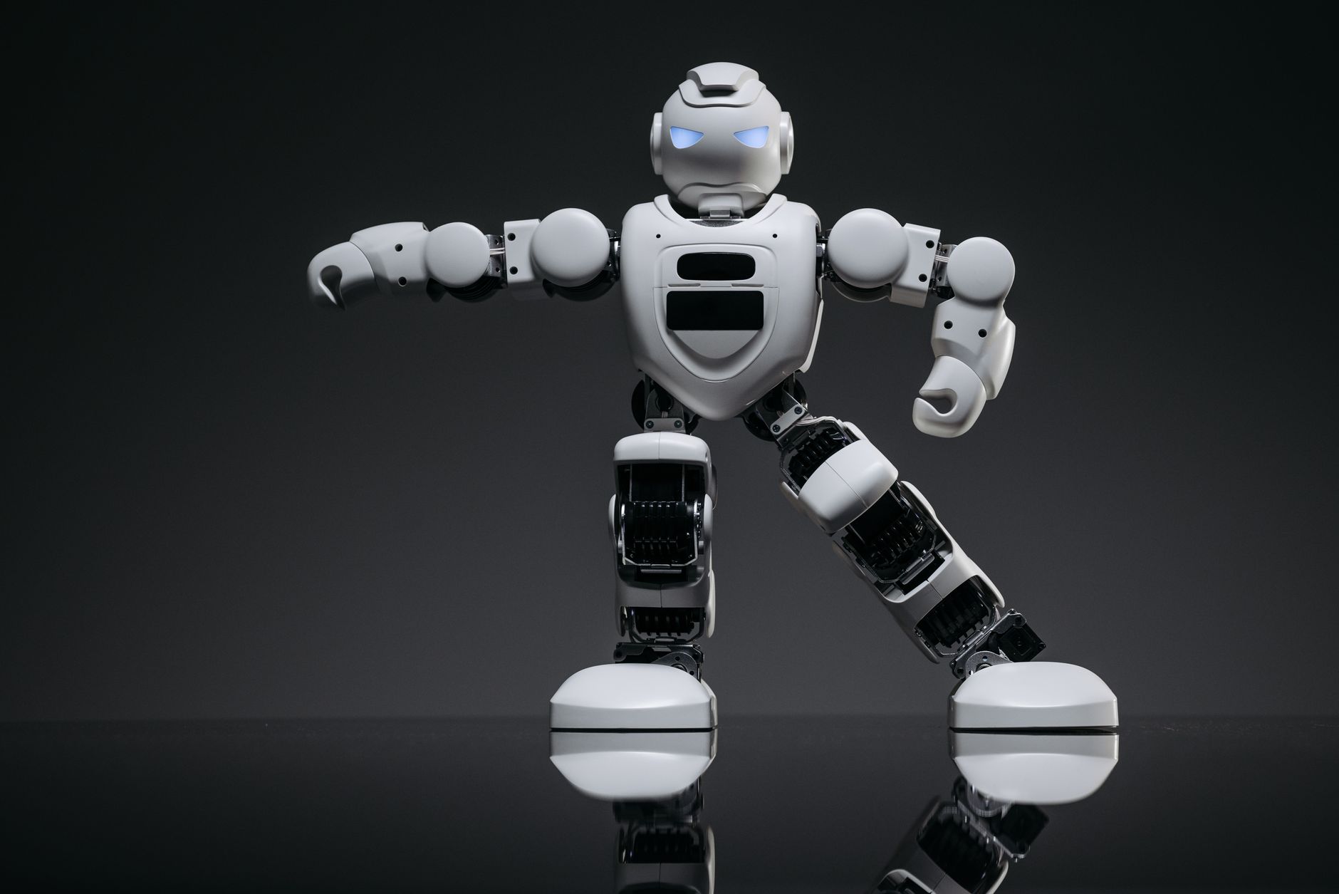 Close-up of a white toy robot with glowing eyes on a reflective black surface.