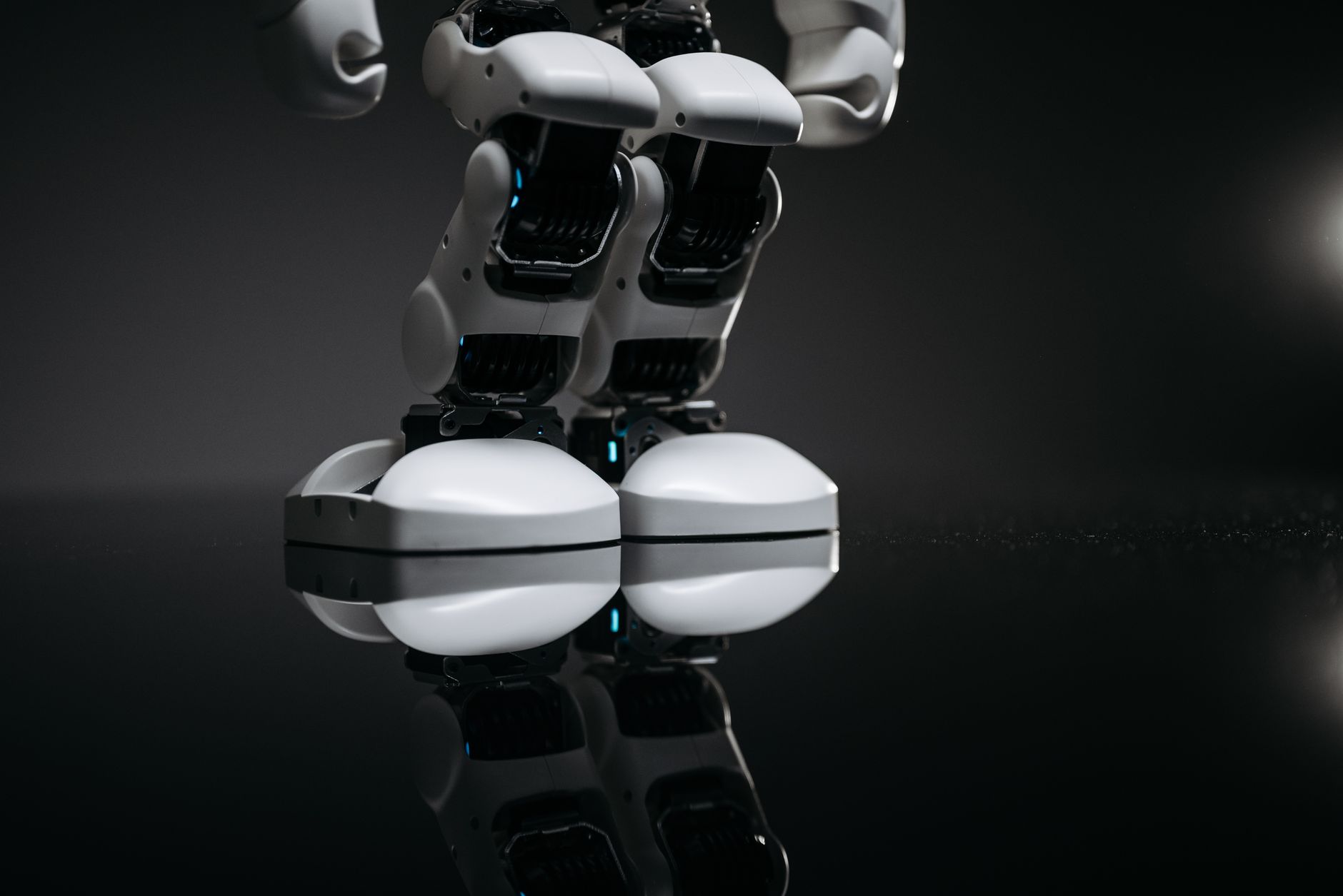 Close-up of robotic legs reflecting on a glossy surface in a studio setting.