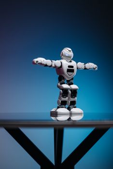 A white humanoid toy robot with raised arms on a glass table, against a blue gradient backdrop.