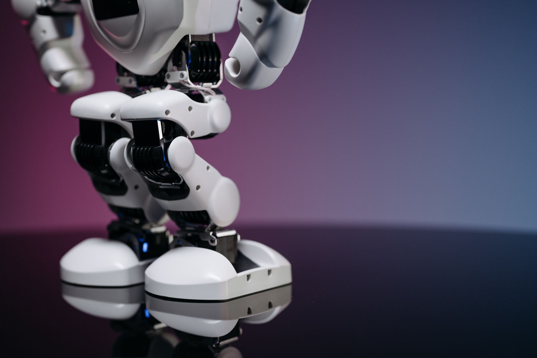 A detailed close-up image of a modern robot's legs and feet, reflecting on a glossy surface.