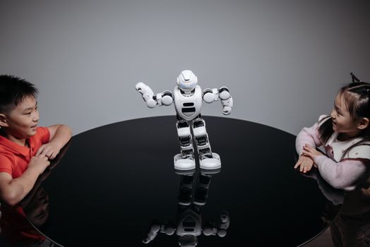 Two children interacting with a robot toy on a table indoors, showcasing technology and fun.