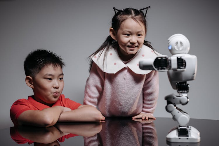 A Young Girl And Boy Looking At The Robot On The Table