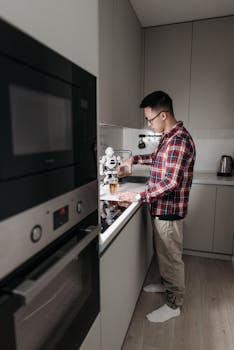 A man in plaid shirt using a robot assistant to pour a beverage in a modern kitchen.