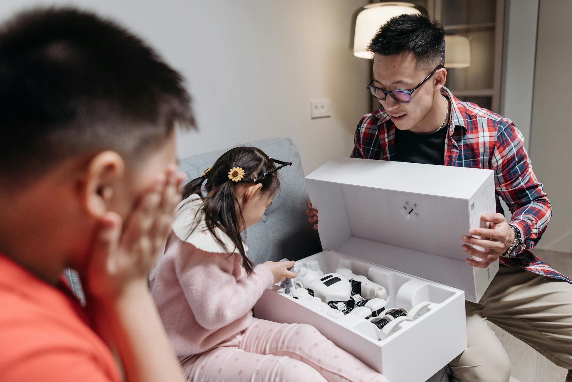 A father and his children excitedly unbox a high-tech robot toy at home.