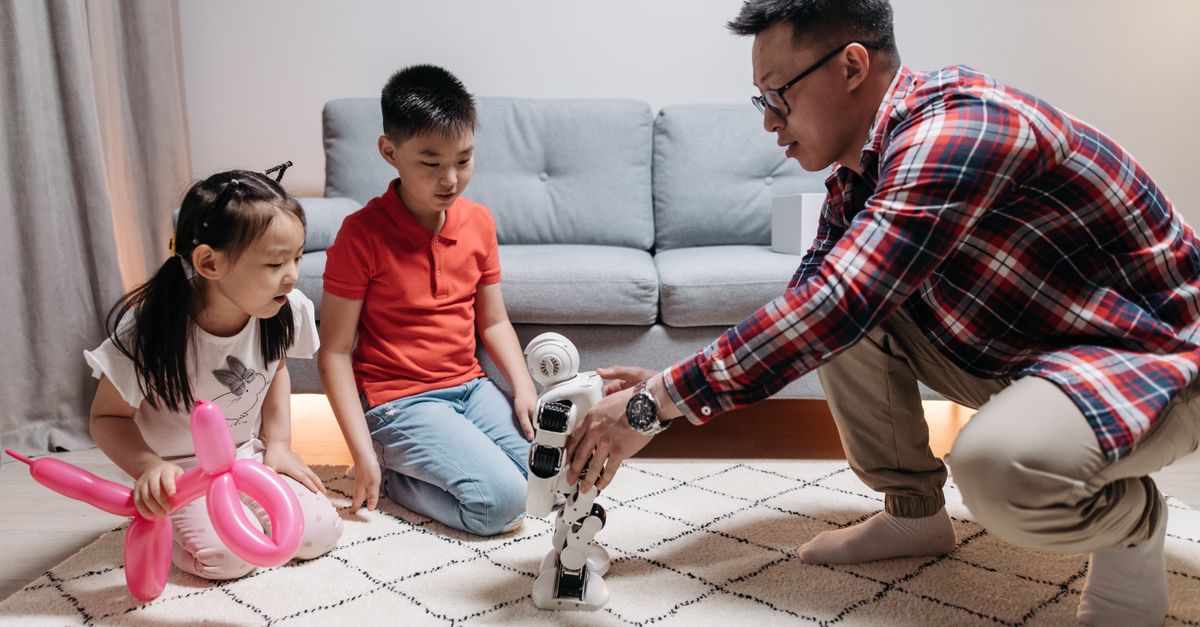Father and children playing with a robot indoors, showcasing family and technology.