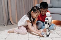 Two Children Sitting on a Rug Playing With a White Robot