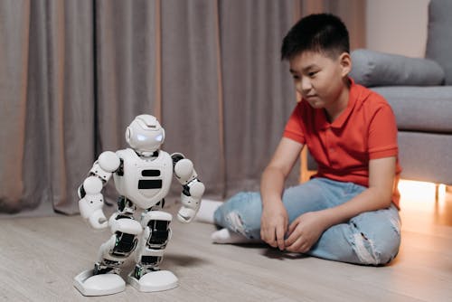 Free A Boy Sitting on the Floor while Looking at the Robot Standing in front of Him Stock Photo