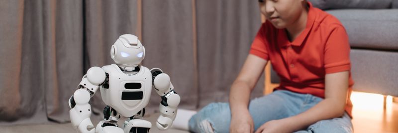 An asian boy sitting on the floor, interacting with a white robot, showcasing innovation and technology.