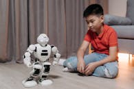 A Boy Sitting on the Floor while Looking at the Robot Standing in front of Him