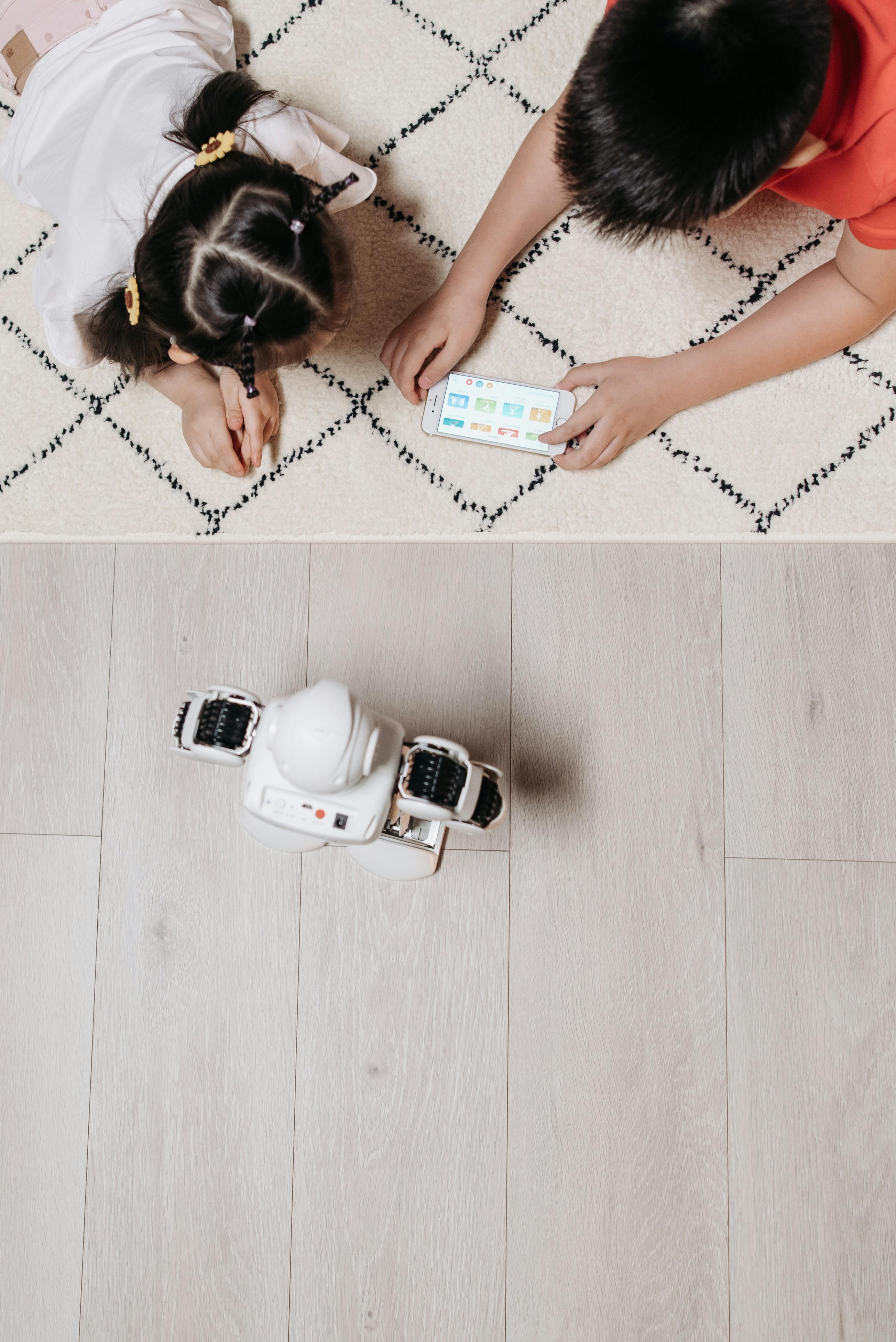 Two children using a remote control to play with a robot indoors.