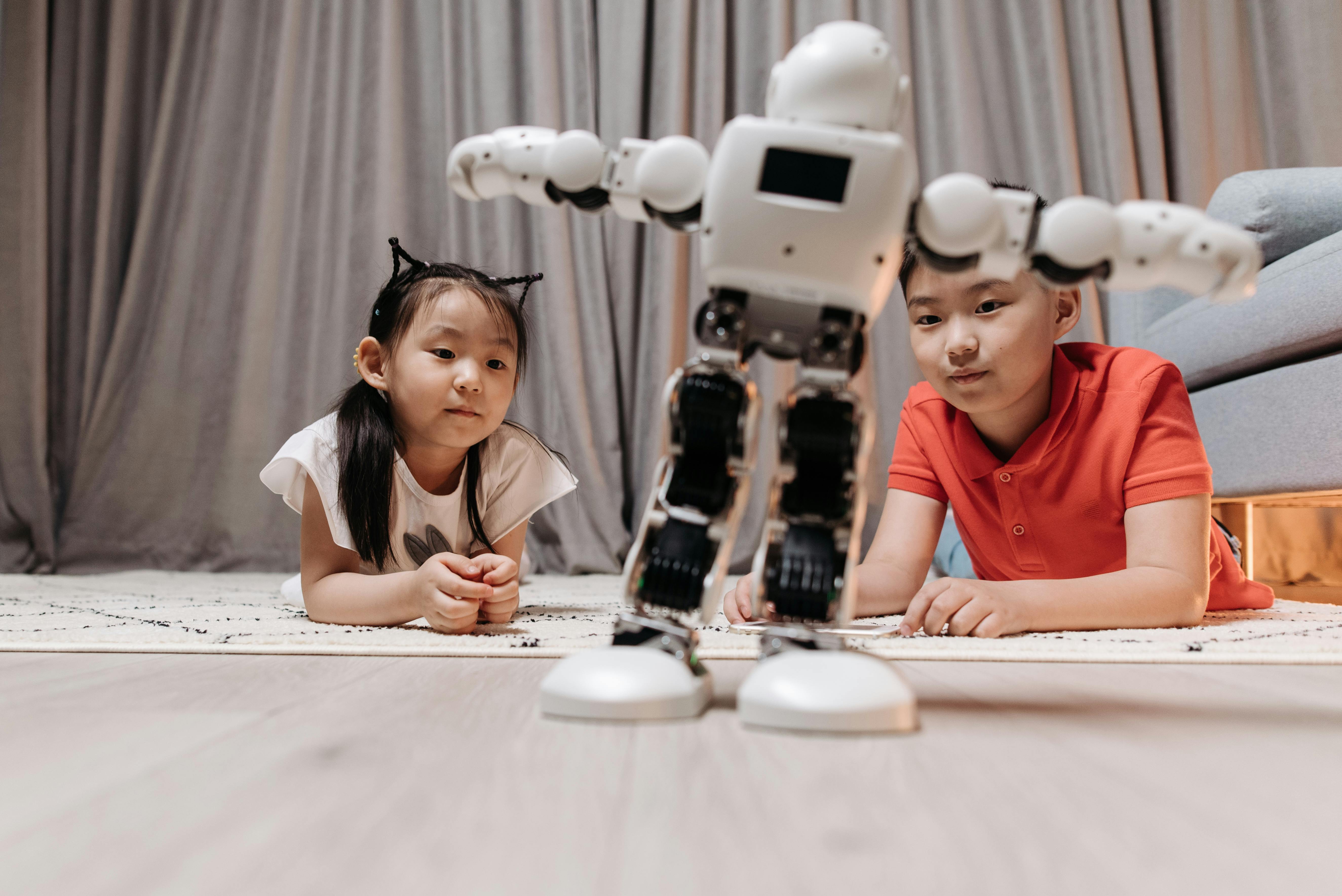 a girl and a boy lying on the floor watching a toy robot