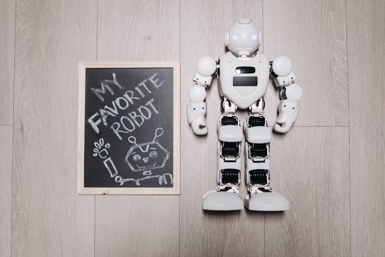 White Robot On A Wooden Flooring Beside A Wooden Board