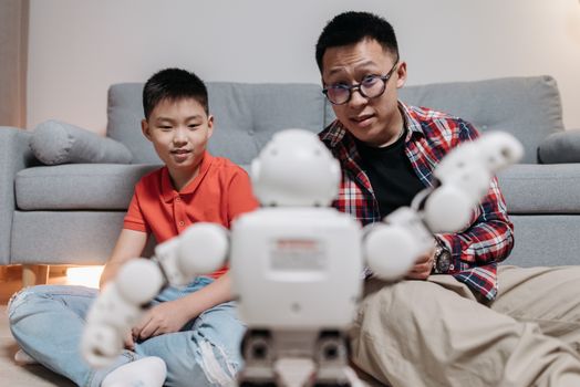 A father and son interact with a robot in a cozy living room, showcasing modern technology and family bonding.
