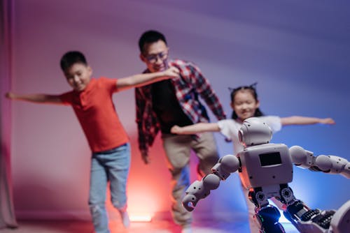 A Man and Two Children Playing With a White and Black Toy Robot