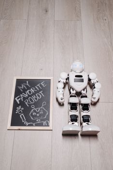 Robot next to chalkboard on a wooden floor, showcasing innovation and art.