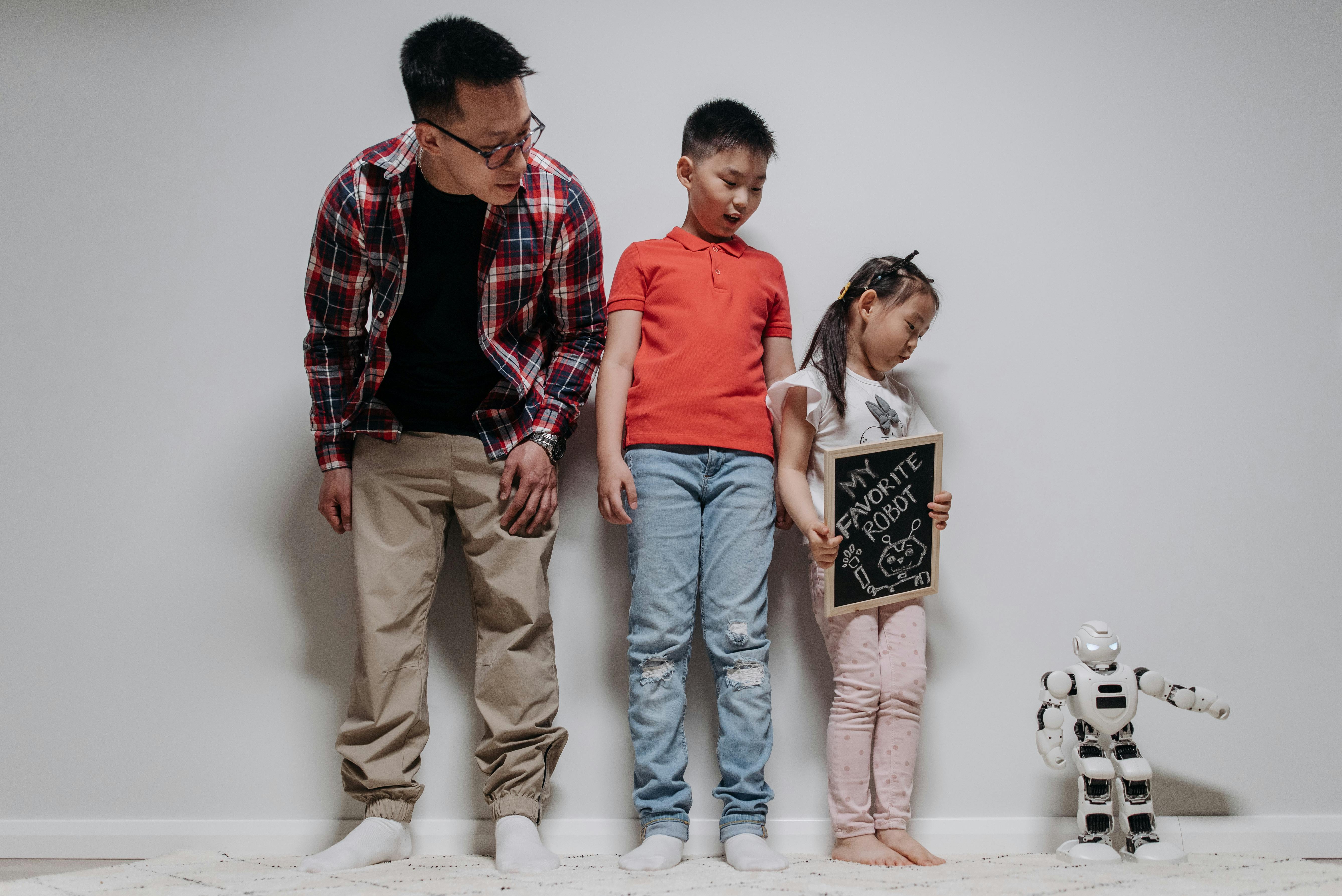 a man two children and a white plastic toy robot standing against a white wall