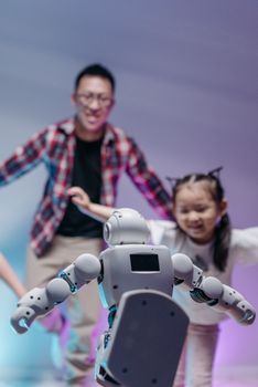 A father and daughter joyfully interact with a small humanoid robot indoors, highlighting fun and technology.