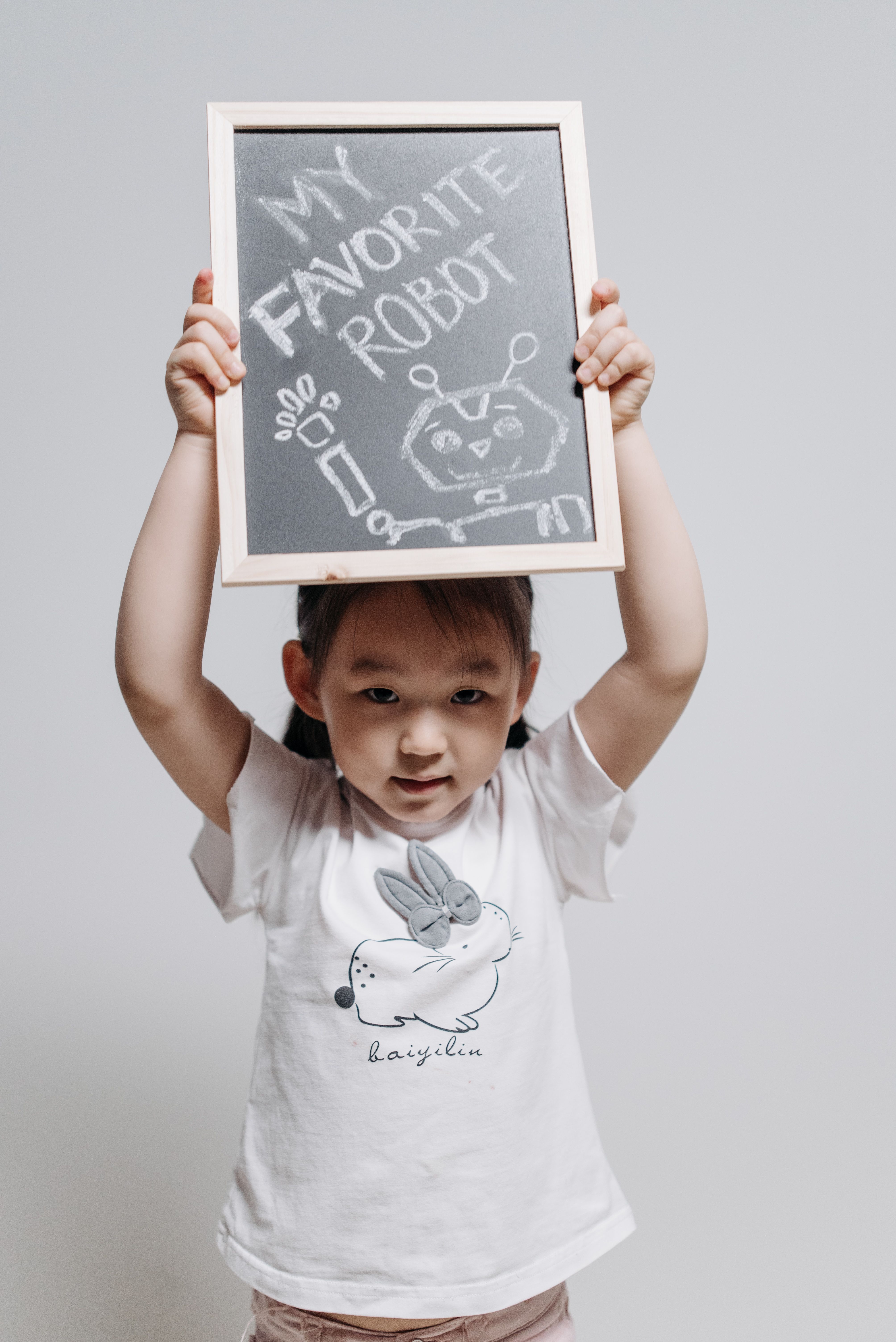 Cute child holding a blackboard with a robot drawing, expressing creativity and innocence.