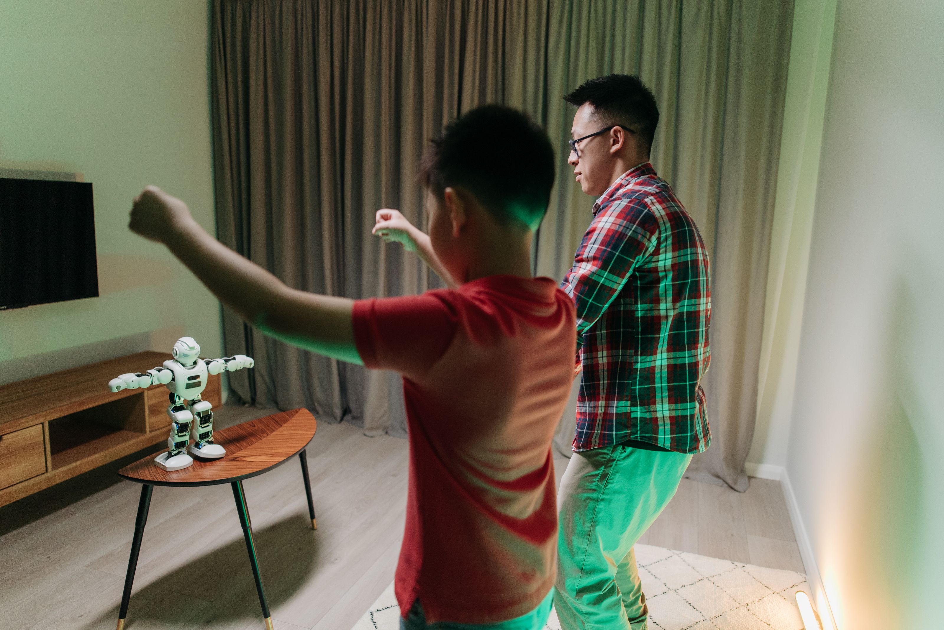 Father and son bonding by dancing with a robotic companion in their living room.