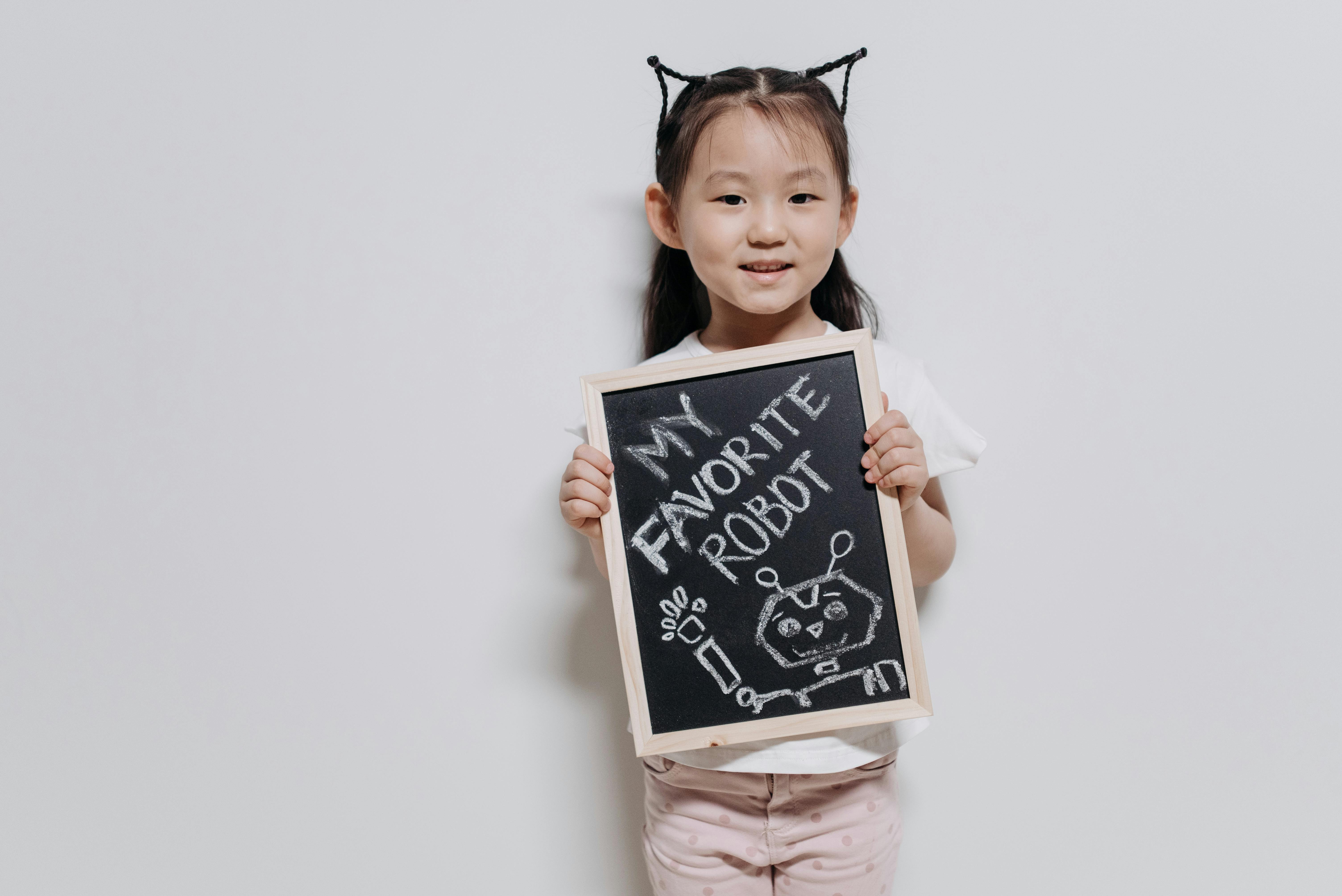 A happy child holding a chalkboard with a robot drawing on a white background.
