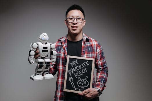 Smiling young man in plaid shirt holding a robot and chalkboard with text 'My Favorite Robot'.