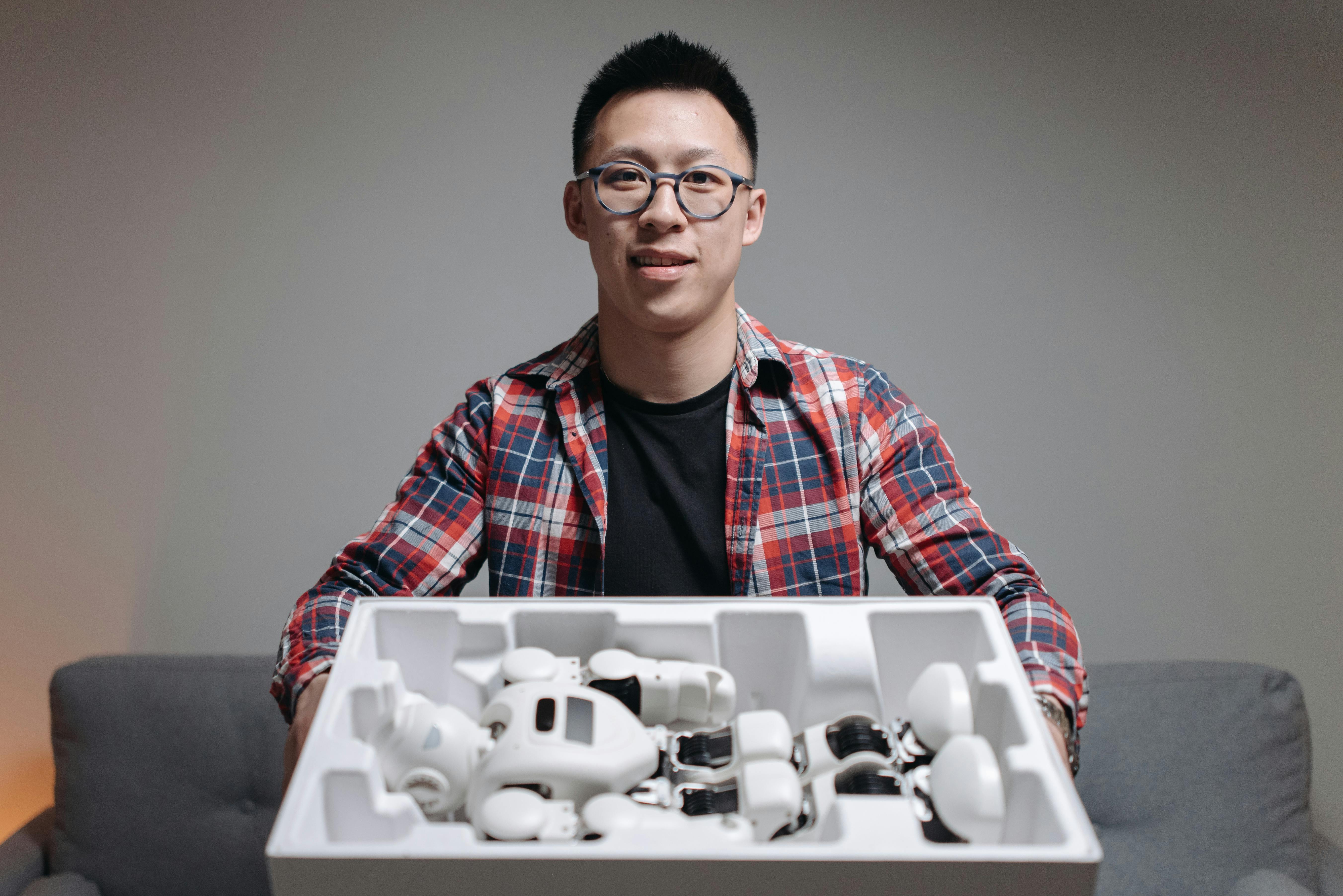 Asian man holding a box with robot components, showcasing technology and innovation indoors.