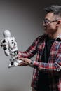 A Man in Plaid Long Sleeves Looking at the Robot he is Holding