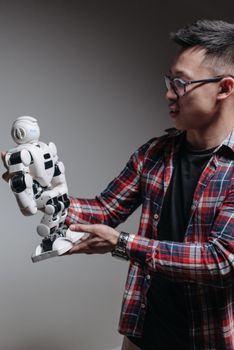 An adult man examines a humanoid robot against a gray background, exploring modern technology.