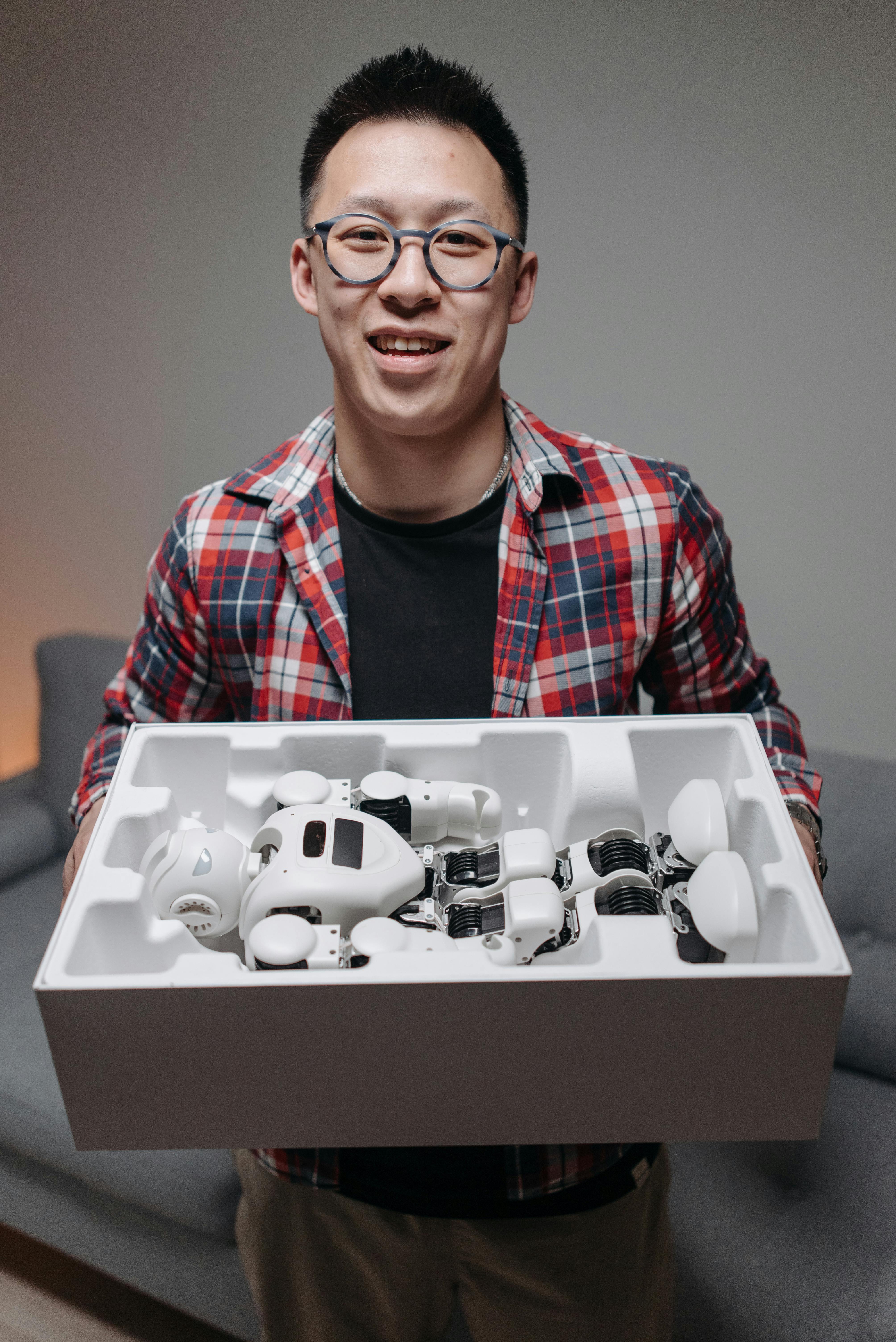 a man wearing checkered shirt and eyeglasses holding a robot toy in a box