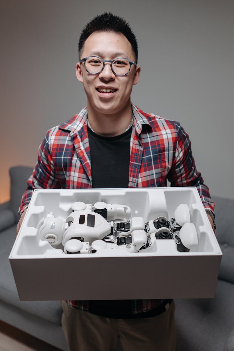 A Man Wearing Checkered Shirt And Eyeglasses Holding A Robot Toy In A Box