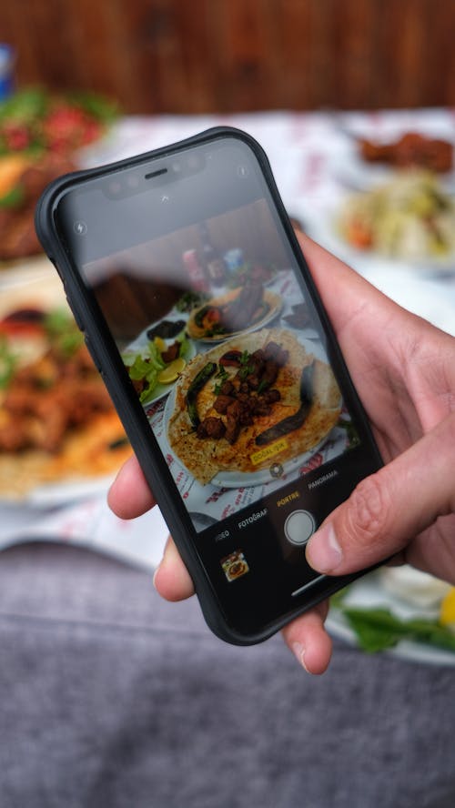 Hand of a Person Holding a Smartphone Taking a Photo of Food