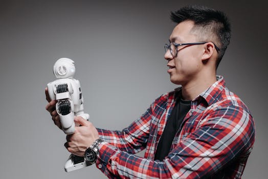 Asian man with glasses in plaid shirt holding a robot toy indoors. Studio shot.