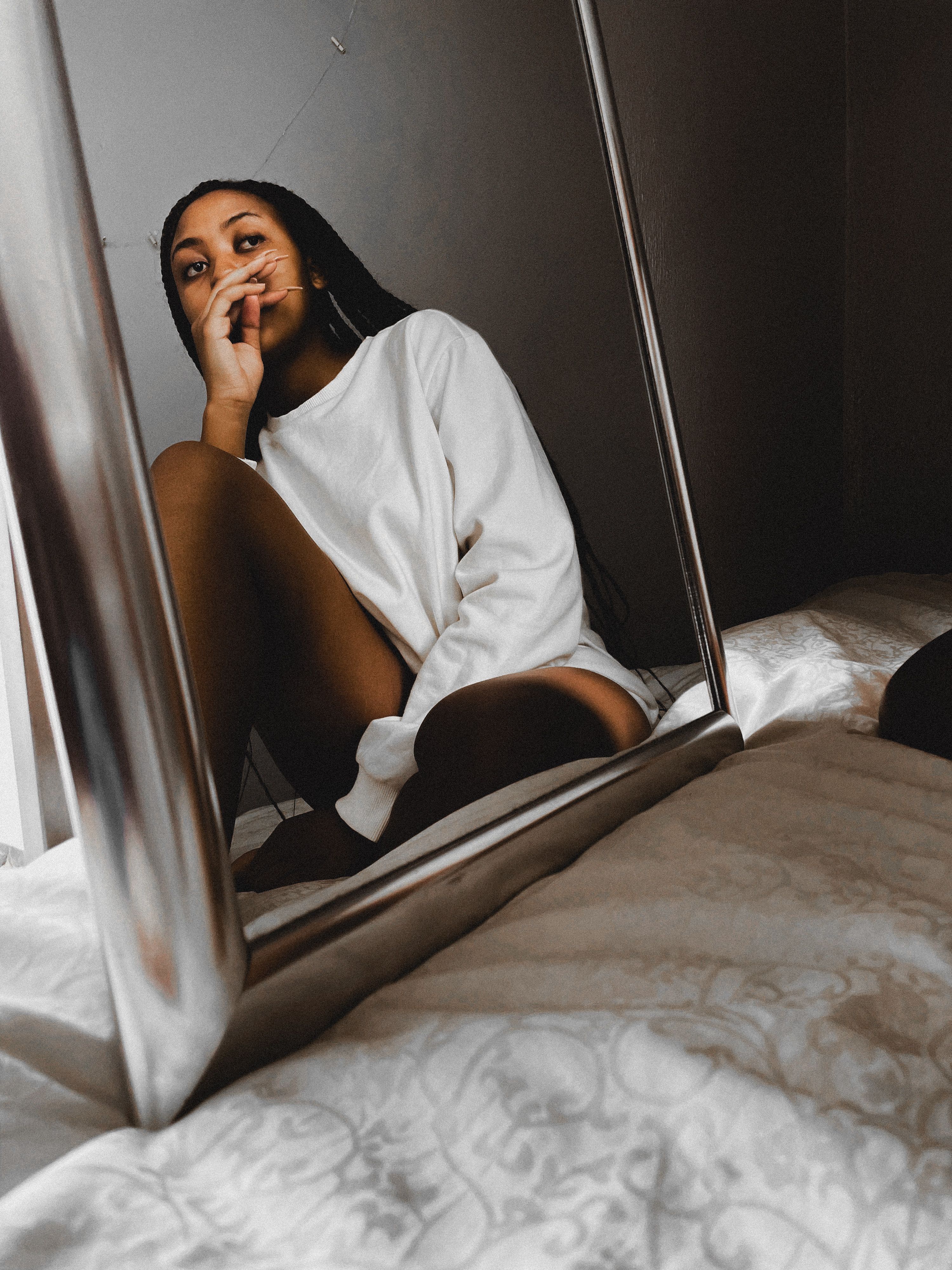 A woman sitting in front of a mirror, reflecting a thoughtful expression in a relaxed indoor setting.