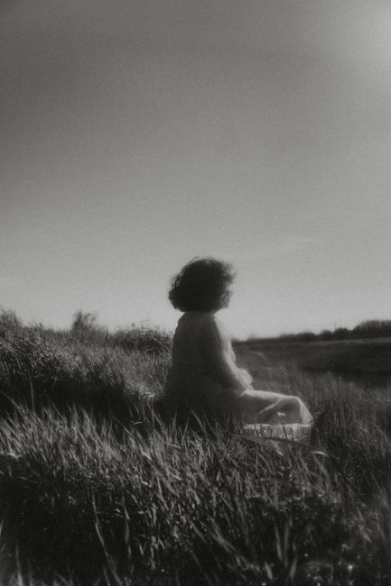 Black and white image of person sitting outdoors on grassy field, bathed in natural light.