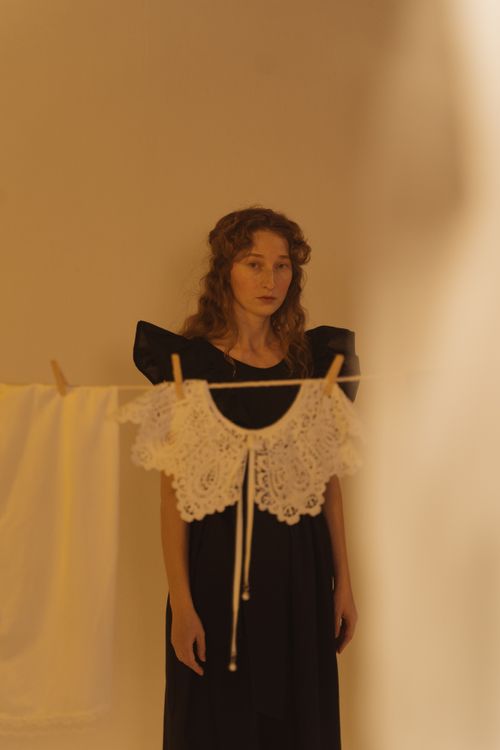 Free A woman in a black dress standing indoors behind lacy clothing on a line. Stock Photo