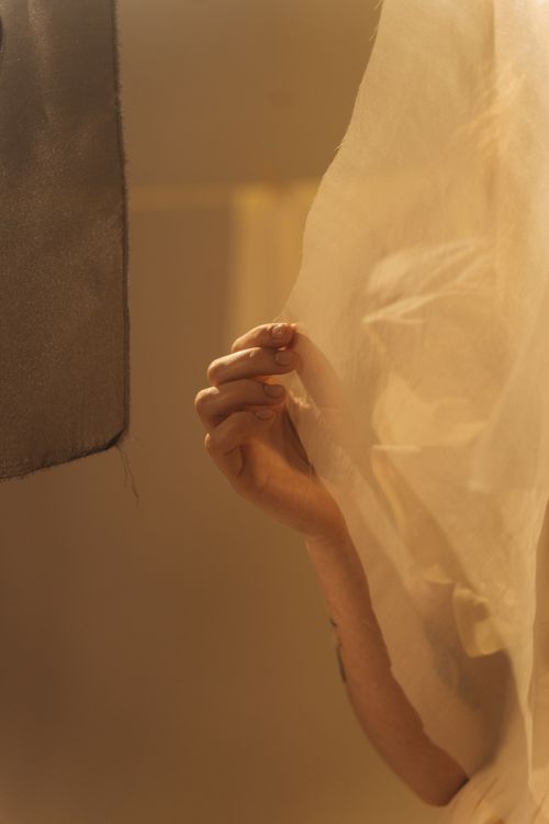 Free A hand gently holding a sheer fabric, creating a soft, warm scene. Stock Photo