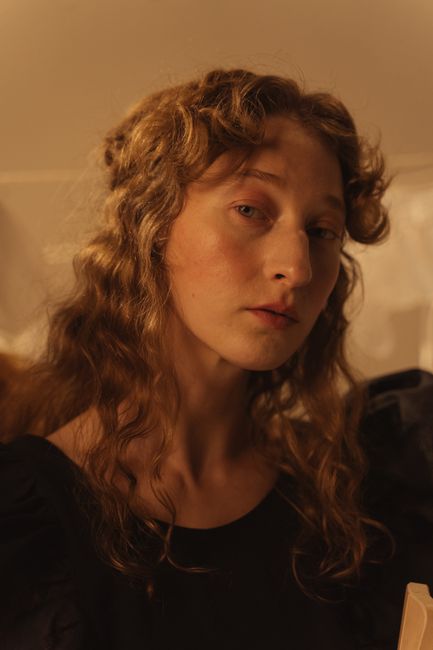 A contemplative portrait of a woman with long curly hair, captured in sepia tones, looking thoughtfully at the camera.