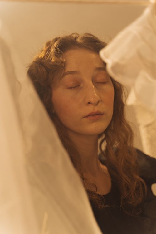 Free A serene close-up of a woman with closed eyes surrounded by delicate lace fabric. Stock Photo