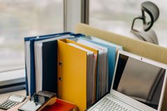 Modern workplace setup with laptop, folders, and gadgets by a window view.