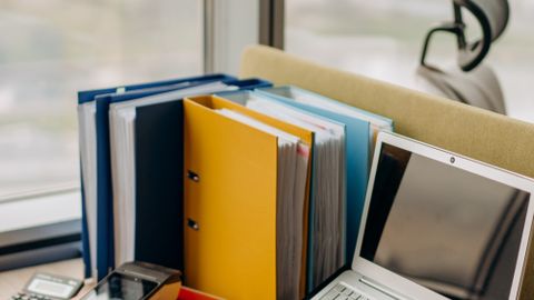 Modern workplace setup with laptop, folders, and gadgets by a window view.