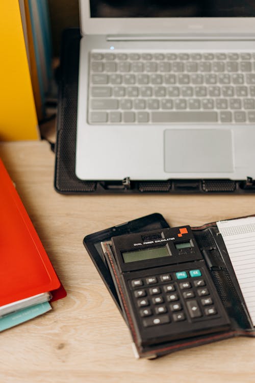 A Laptop Beside a Calculator on a Wooden Table