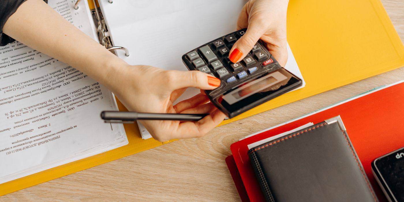 Hands using a calculator at a desk with documents and folders, ideal for finance or accounting themes.