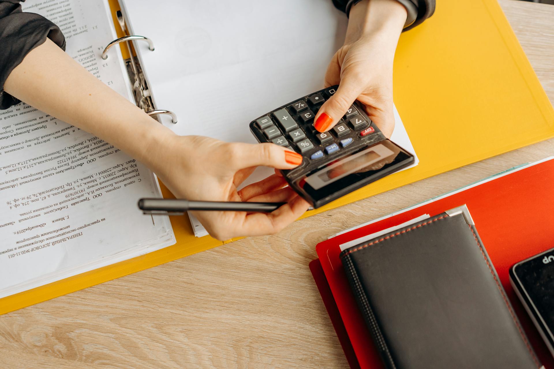 Hands using a calculator at a desk with documents and folders, ideal for finance or accounting themes.