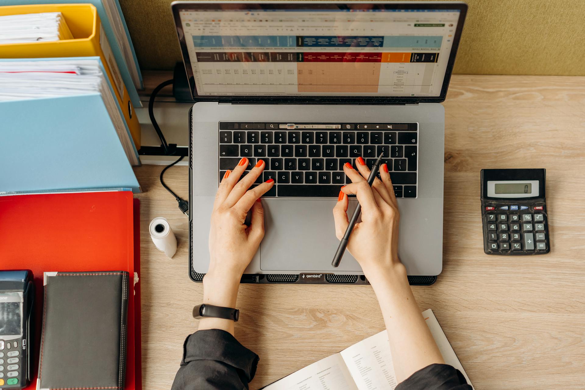 Top view of hands typing on laptop at a desk with folders and calculator.